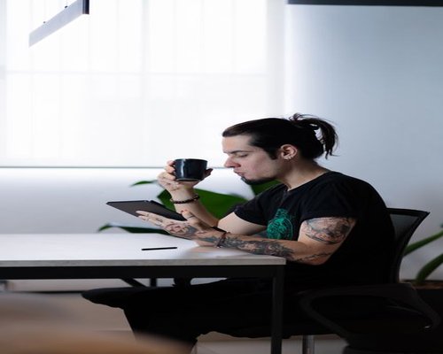 Young creative professional drinking coffee and reading next to a bright window in an open office space in Guadalajara
